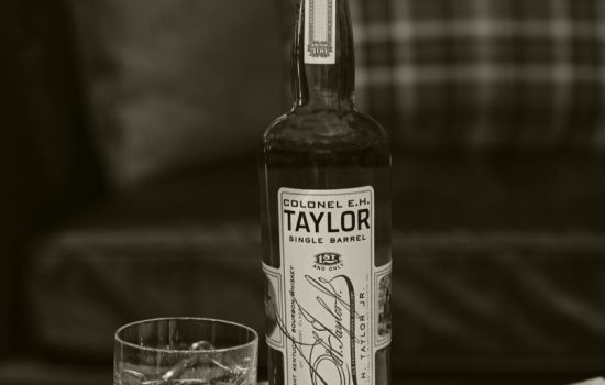 A whiskey glass with a unopened bottle of Colonel E.H. Taylor Single Barrel Straight Kentucky Bourbon Whiskey