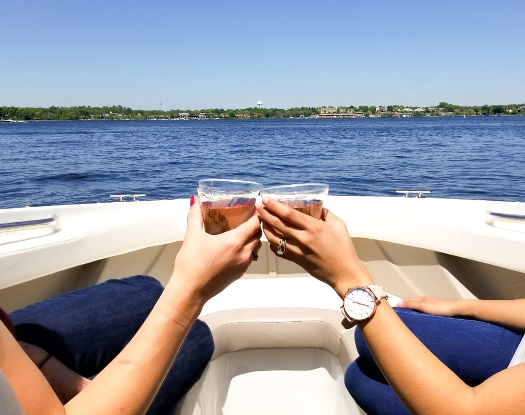 Friends toasting with wine glasses on a boat, blue water and sky in the background.