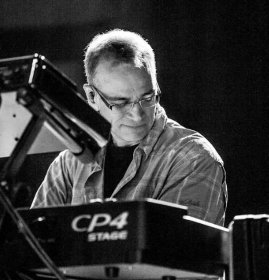 Black-and-white photo of a man wearing glasses playing a CP4 Stage keyboard on stage, focused on the instrument.