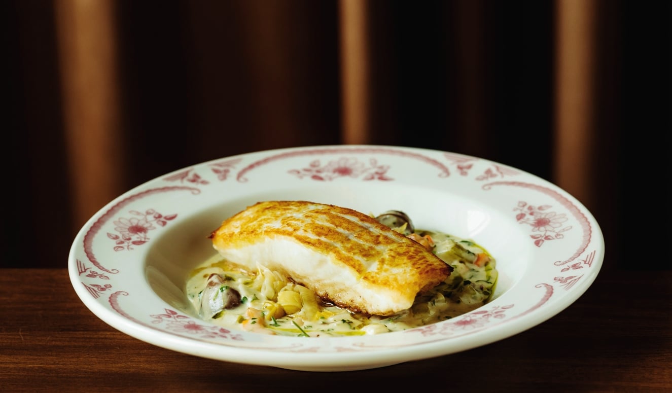 Pan-seared fish fillet atop a bed of creamy vegetable sauce on a white plate with a red floral pattern