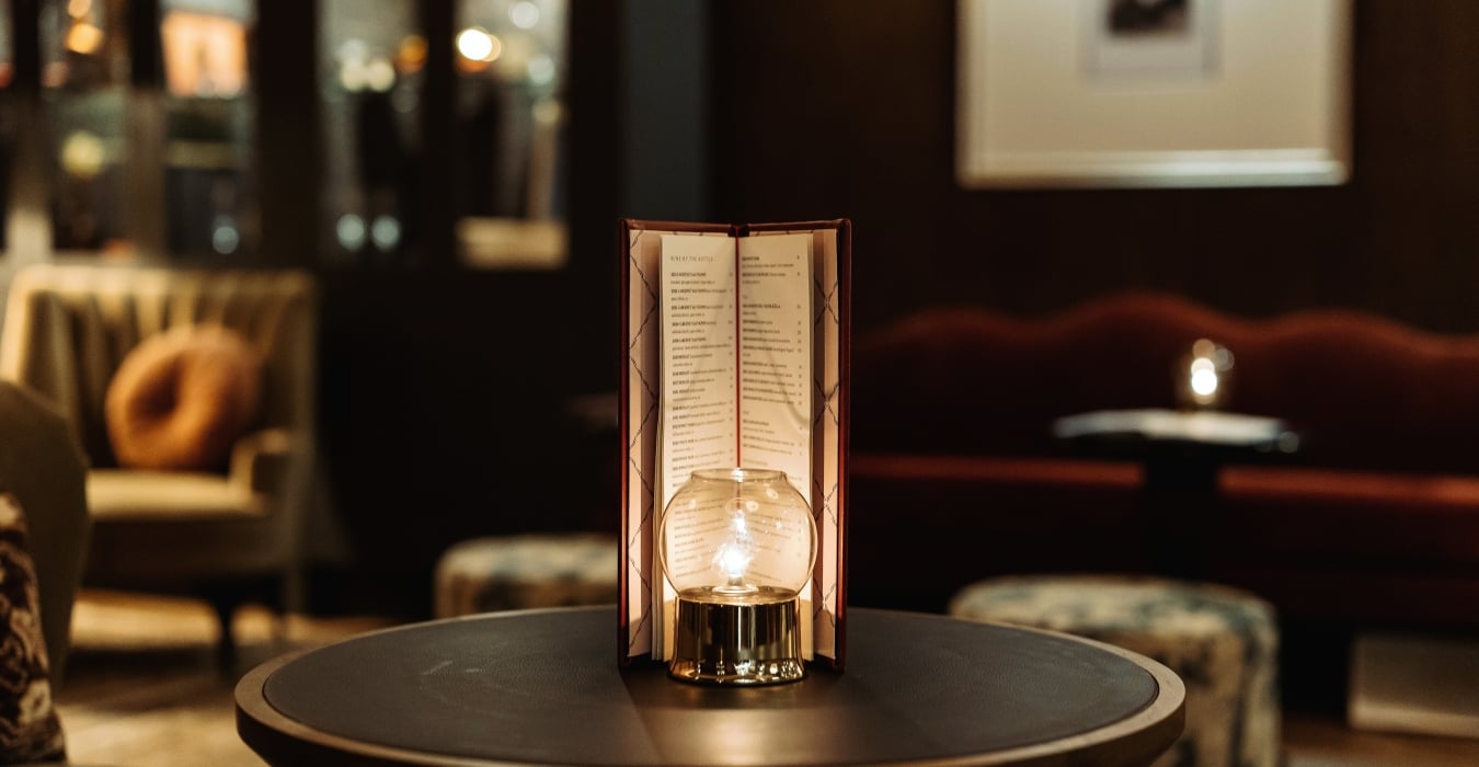Menu card stand on a table in a dim, candlelit restaurant setting with a glowing bulb nearby.