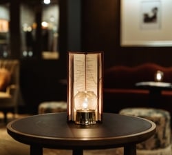 Menu card stand on a table in a dim, candlelit restaurant setting with a glowing bulb nearby.