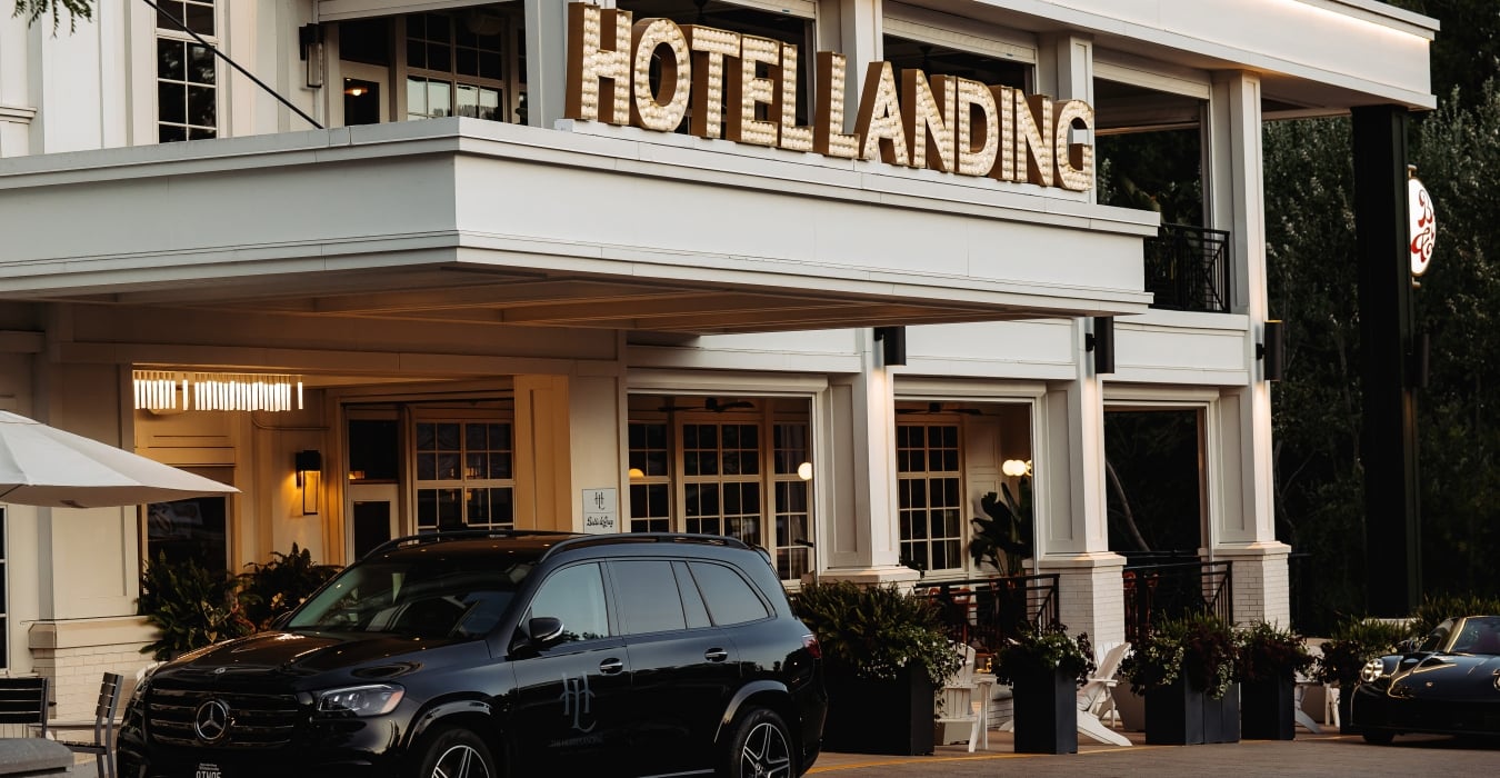 Exterior of Hotel Landing with a large illuminated sign reading 'HOTEL LANDING' and a black Mercedes SUV in the foreground.