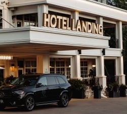 Exterior of Hotel Landing with a large illuminated sign reading 'HOTEL LANDING' and a black Mercedes SUV in the foreground.
