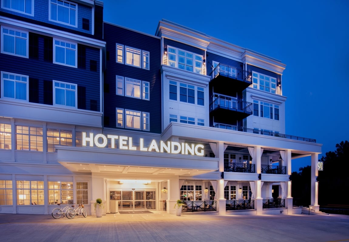 Modern multi-story hotel facade at dusk with lit windows and balconies; neon sign reads HOTEL LANDING at entrance area.