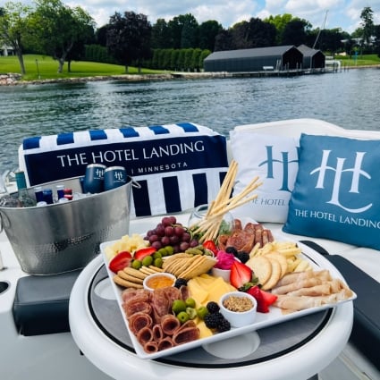 Charcuterie board on a boat deck with Hotel Landing branded pillows, overlooking a calm lake