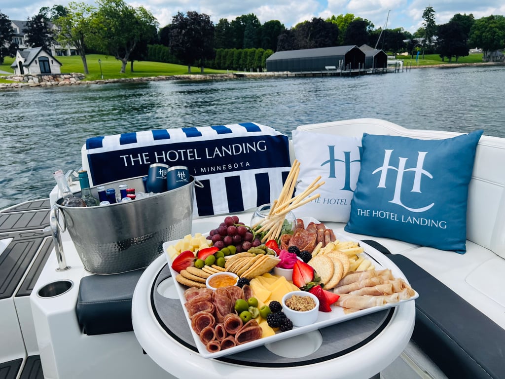 Charcuterie board on a boat deck with Hotel Landing branded pillows, overlooking a calm lake