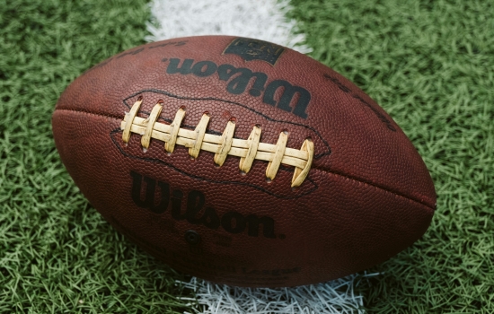 Close-up of a brown Wilson football resting on green artificial turf with a white painted line nearby.