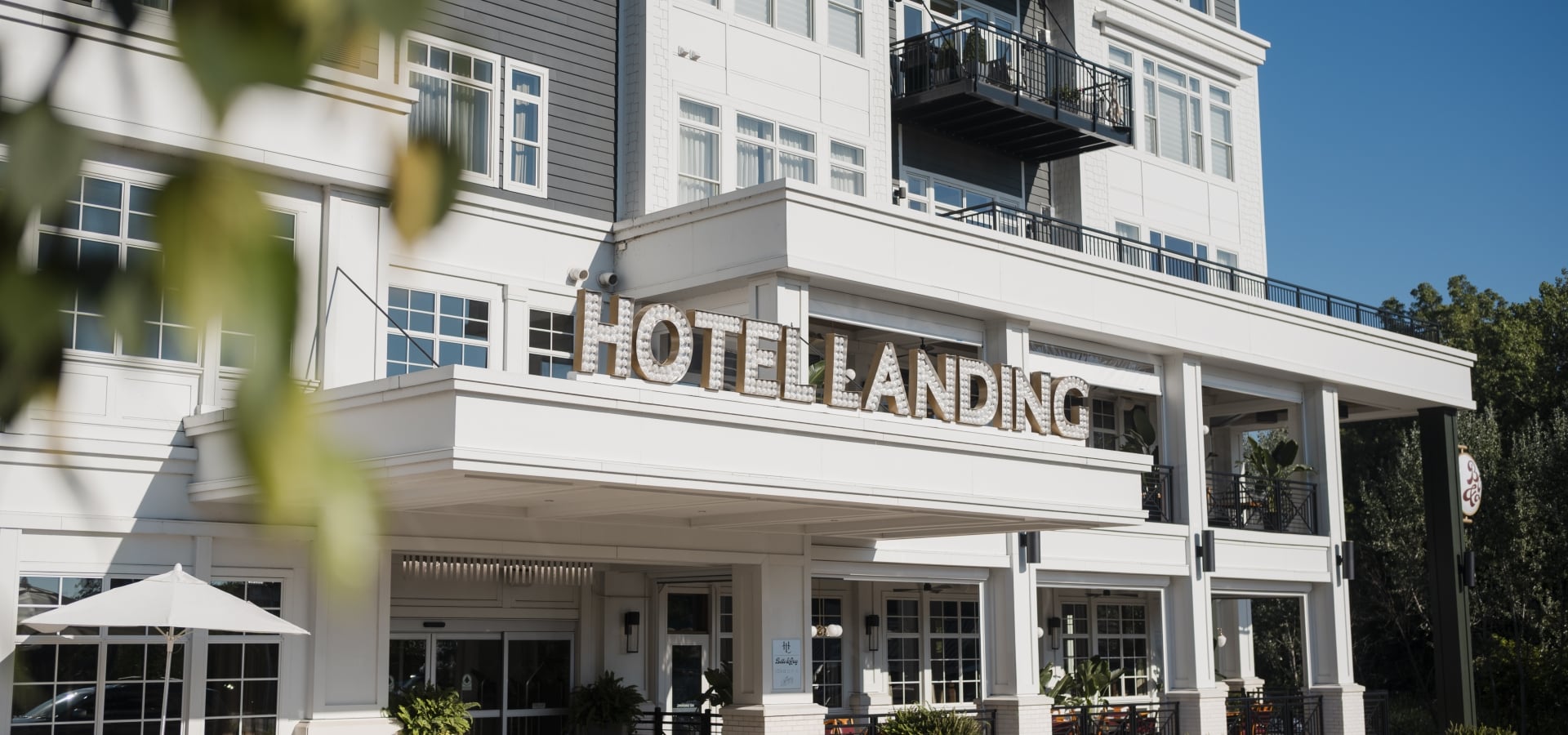 Hotel entrance facade with large sign 'HOTEL LANDING' and outdoor seating under white awning, blue sky above.