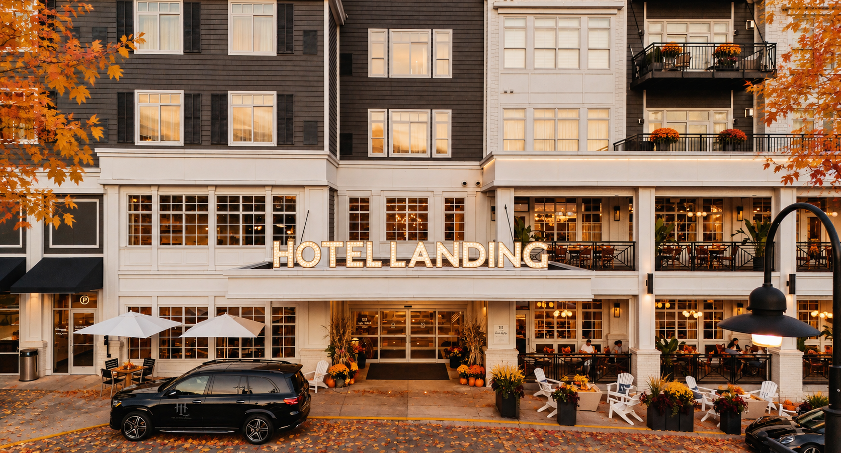 Hotel Landing exterior at dusk with a lit marquee sign, white facade, and outdoor dining on the ground and balcony levels amid autumn leaves.