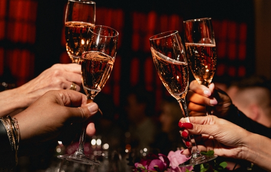 People clinking champagne flutes in a festive toast over a table with pink flowers in the foreground