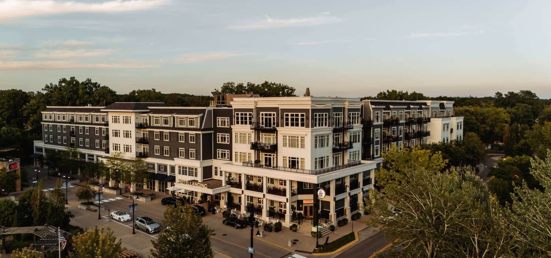 Modern mixed-use apartment building with balconies, street-level shops, and surrounding trees in an urban setting.