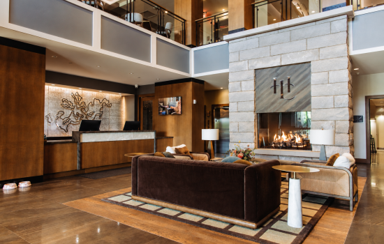 Hotel lobby with a large stone fireplace and modern seating area, brown leather sofas, and a reception desk to the left.